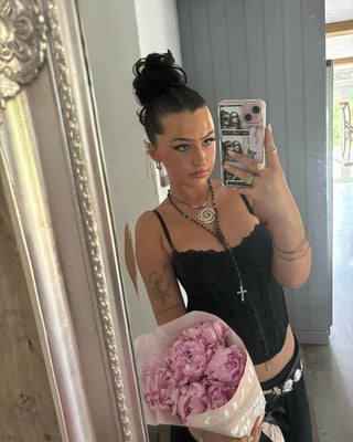 Young person in mirror selfie holding peony flower bouquet, showcasing stylish outfit and accessories.